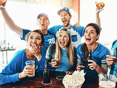 People gathered around a bar in matching sports gear cheering and drinking