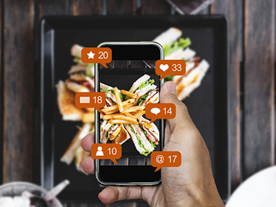 Top view of a person taking a photo of a meal with their cellphone, with graphics of social media notifications around the phone