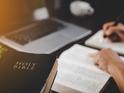 A person studying the bible near a laptop