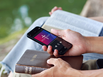 A pair of hands holding a Bible and a phone with a audio track called 