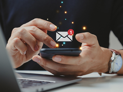 Person's hands on a cellphone with an email notification graphic floating above it 