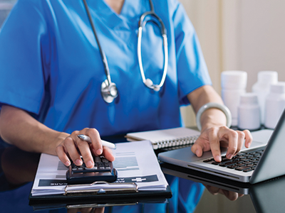 Healthcare professional sitting at laptop calculating bill for patient