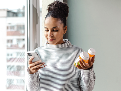 Woman looking at her phone while holding two pill bottles