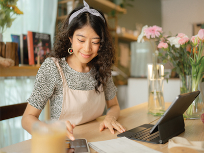 Woman in her store calculating profit on her phone and laptop/POS