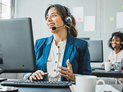 A woman sitting at a desk on a computer with a headset and microphone on offering customer service