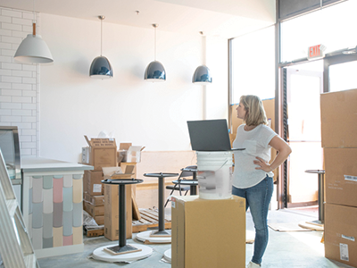 A woman in her new retail building with boxes and ladders ready to unpack and set up her store