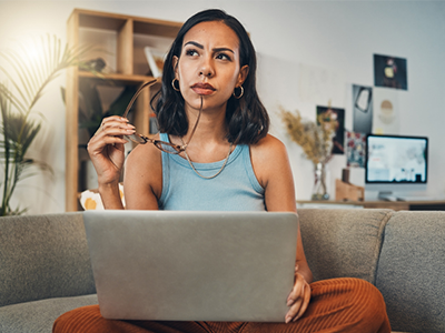 Woman sitting on a sofa with a laptop, looking in the air as if thinking about something