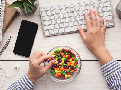 A top-down view of a work desk with hands reaching into a bowl of Skittles like candy