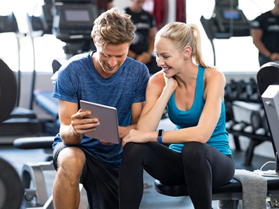 A fitness trainer showing a gym member a routine on a tablet