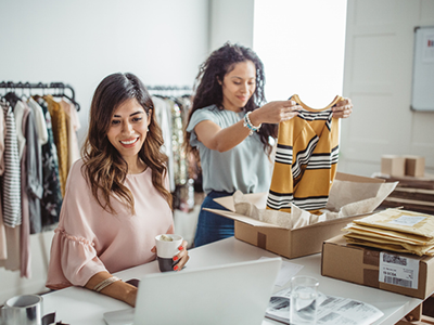 Two women working in a clothing store on a laptop and folding clothes