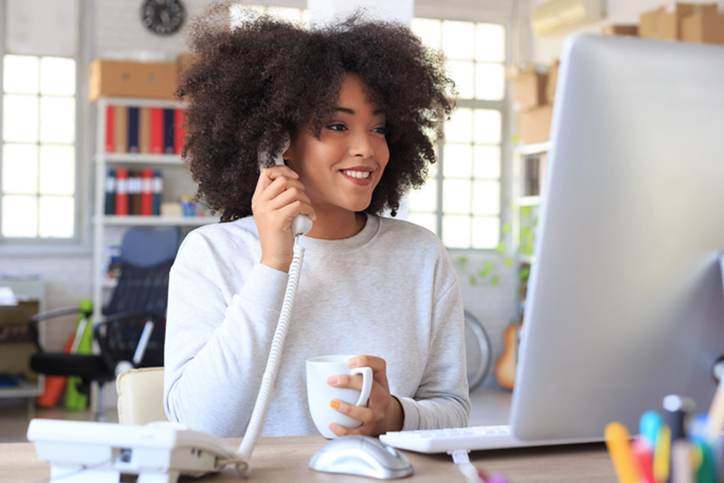 Woman sitting at a computer in an office talking on a work phone.