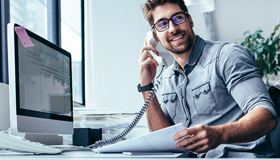 Man sitting at computer desk in an office talking on a work phone
