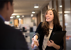 Woman in business attire shaking hands with a man in suit faced away from the camera