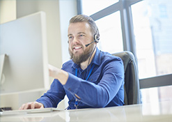 Man in blue button up with headset and mic looking and pointing at a computer screen
