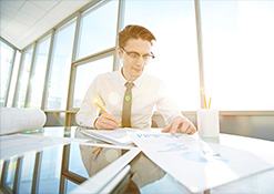 Man wearing glasses in business attire looking at papers on a table